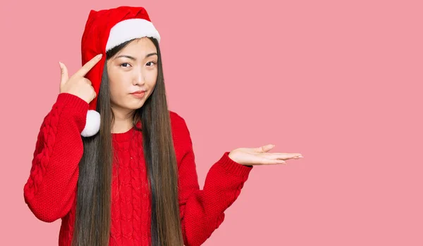 クリスマスの帽子を身に着けている若い中国の女性は混乱し コピースペースを示し 額に指を指すオープンパームに悩まされる 考えてみてください — ストック写真