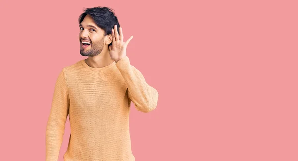 噂やゴシップに耳を傾ける耳の上に手で笑みを浮かべてカジュアルなセーターを着てハンサムなヒスパニック系の男 聴覚障害の概念 — ストック写真