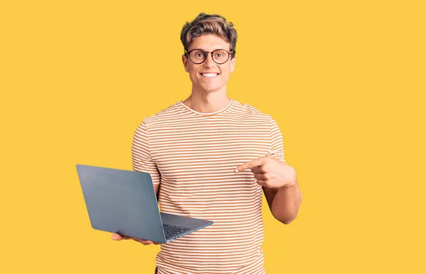 年轻英俊男子戴着眼镜 手持笔记本电脑 面带微笑 手指手画脚 — 图库照片