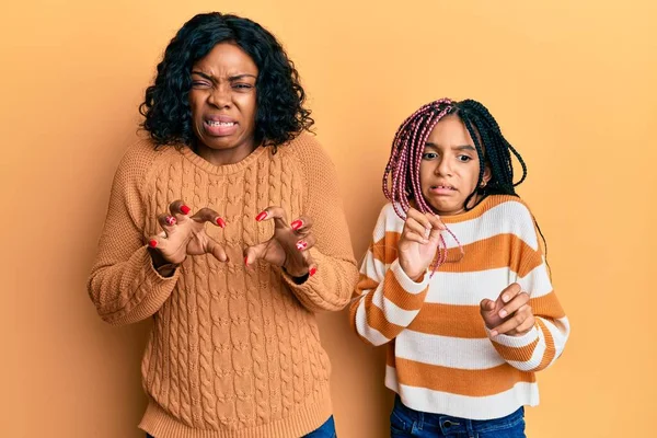 Beautiful african american mother and daughter wearing wool winter sweater disgusted expression, displeased and fearful doing disgust face because aversion reaction.