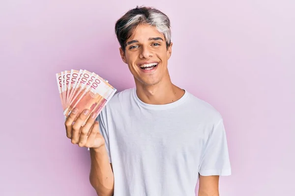 stock image Young hispanic man holding 100 norwegian krone banknotes looking positive and happy standing and smiling with a confident smile showing teeth 