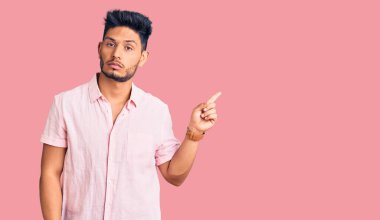 Yakışıklı Latin Amerikalı rahat bir yaz tişörtü giyen genç adam. El parmağı yanda, ciddi ve sakin bir yüz ifadesi sergiliyor. 