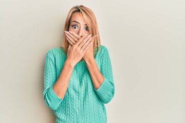 Kış süveteri giyen güzel sarışın kadın yanlışlıkla elleriyle ağzını kapatırken şok oldu. gizli kavram. 