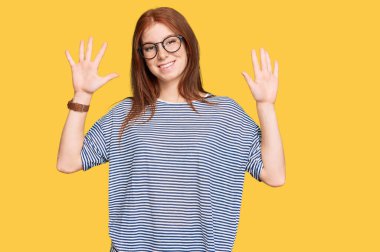 Gündelik kıyafetler giyen, gözlüklü genç bir kadın on numarayı gösterip işaret ederken kendinden emin ve mutlu gülümsüyor.. 