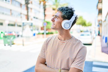 Genç, yakışıklı, beyaz, gülümseyen, müzik dinleyen, kulaklık takan, şehirde yürüyen bir adam..