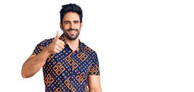 Yakışıklı İspanyol adam günlük kıyafetler giyiyor mutlu ve pozitif gülümsüyor, başparmağıyla mükemmel ve onay işareti yapıyor. 