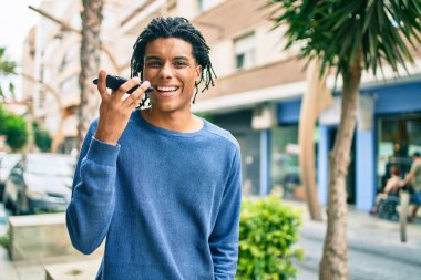 Genç Afrikalı Amerikalı adam şehrin caddesinde akıllı telefon kullanarak mutlu gülümsüyor..