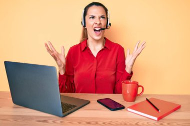 Çağrı merkezinde operatör kulaklığı takan genç esmer kadın kızgın, deli gibi bağırıyor ve agresif bir ifade ve kollar havada bağırıyor. hüsran kavramı. 