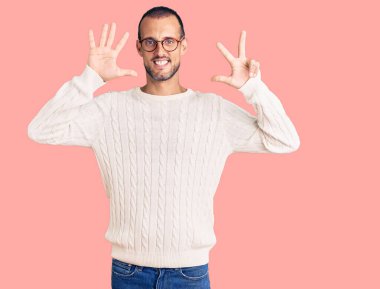 Genç yakışıklı adam, günlük kıyafetler ve gözlük takıyor. Sekiz numaralı parmaklarıyla gösteriyor ve işaret ediyor. Kendinden emin ve mutlu bir şekilde gülümsüyor.. 