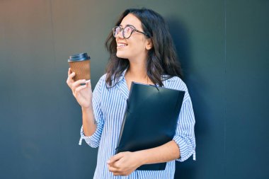 Latin kökenli genç bir iş kadını şehirde kahve içip duruyor.