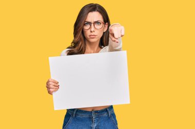 Elinde boş afiş tutan genç esmer kadın kamerayı işaret ediyor ve sen kendine güvenen ciddi bir hareket yapıyorsun. 