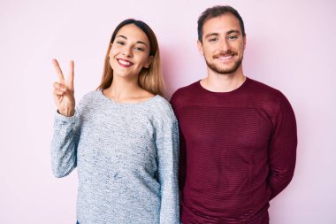 Güzel bir çift gündelik giysiler giyer ve iki numarayı göstererek mutlu ve kendinden emin bir şekilde gülümserler.. 