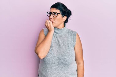 Artı, sıradan kıyafetler ve gözlük takan esmer kadın gergin ve elleri ağız yiyen tırnaklarla gergin görünüyor. anksiyete. 