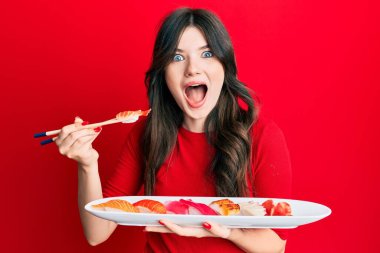 Genç beyaz kız suşi yiyor. Yemek çubuklarıyla deliliği kutluyor. Başarı için hayrete düşüyor.. 