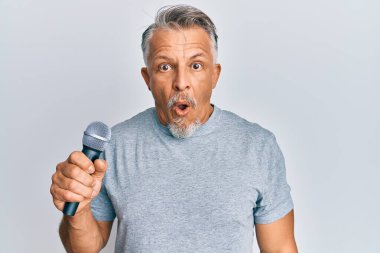 Orta yaşlı, kır saçlı bir adam mikrofon kullanarak şarkı söylüyor. Korkmuş ve ağzı açık bir şekilde şaşırmış, inançsız bir yüz. 