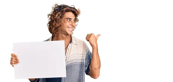 Jovem Hispânico Segurando Banner Vazio Apontando Polegar Para Lado Sorrindo — Fotografia de Stock