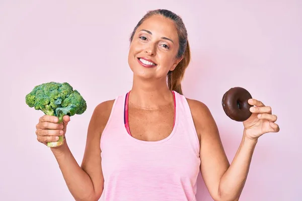 中年时 他惊慌失措的女人牵着花椰菜和巧克力甜甜圈 脸上挂着快乐而清凉的笑容 显示牙齿 — 图库照片