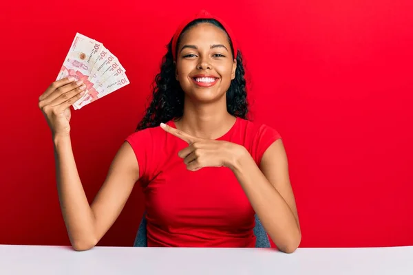 Joven Afroamericana Sosteniendo Billetes Pesos Colombianos Sentada Sobre Mesa Sonriendo —  Fotos de Stock