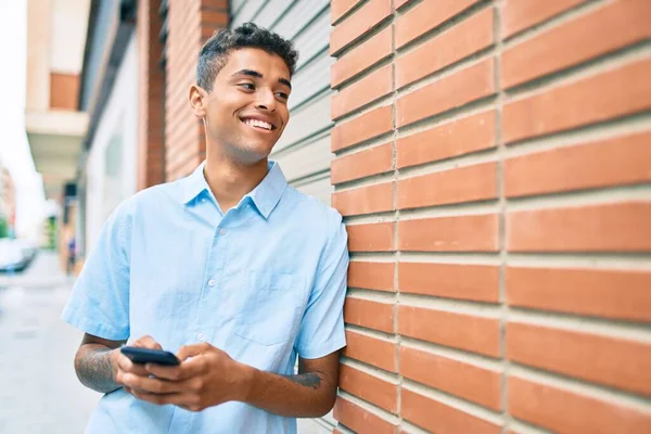 Νεαρός Λατίνος Άνθρωπος Χαμογελά Χαρούμενος Χρησιμοποιώντας Smartphone Ακουμπά Στον Τοίχο — Φωτογραφία Αρχείου