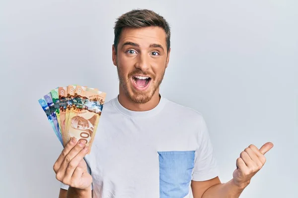 Hombre Caucásico Guapo Sosteniendo Dólares Canadienses Apuntando Pulgar Hacia Lado —  Fotos de Stock