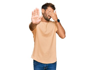 Sakallı, sıradan tişörtler giyen, elleriyle gözlerini kapatan, üzgün ve korku dolu hareketler yapan yakışıklı bir genç. utangaç ve olumsuz kavram. 