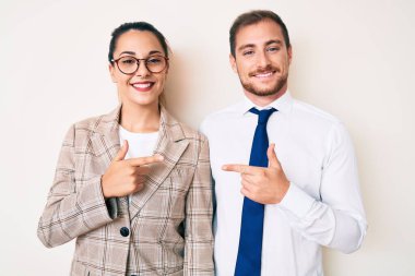 Güzel bir çift iş kıyafetleri içinde neşeli bir gülümseme ile elleri ve parmaklarıyla işaret ederek mutlu ve doğal bir ifadeyle. 