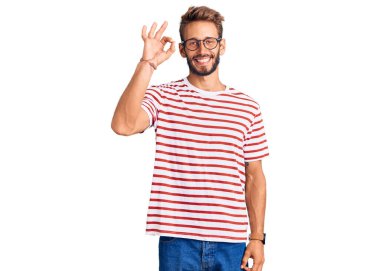 Sakallı, sıradan giyinen, gözlüklü, gülümseyen, el ve parmaklarıyla tamam işareti yapan yakışıklı sarışın adam. başarılı ifade. 