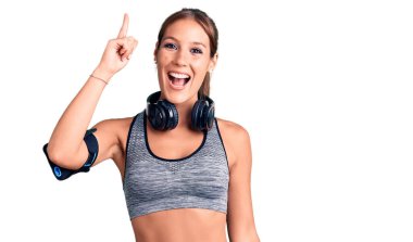 Spor kıyafetleri giyen ve kulaklık takan genç, güzel İspanyol bir kadın başarılı bir fikirle işaret ediyor. Heyecanlı ve mutlu. Bir numara.. 