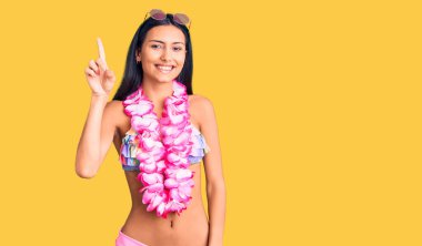 Bikini giyen genç ve güzel bir Latin kız ve Hawaii zambağı başarılı bir fikirle işaret ediyor. Heyecanlı ve mutlu. Bir numara.. 
