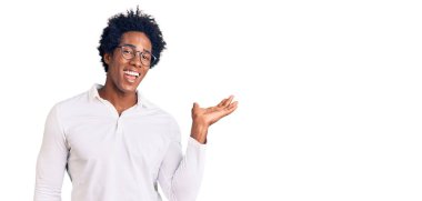 Afro saçlı, sıradan giyinmiş, gözlüklü, neşeli gülümseyen, eli kameraya bakan yakışıklı Afro-Amerikalı adam.. 