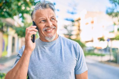 Orta yaşlı, İspanyol, gri saçlı, gülümseyen, mutlu, akıllı telefondan konuşan bir adam..