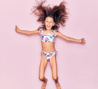 Sevimli İspanyol çocuk tatilde bikini giymiş mutlu bir şekilde gülümsüyor. İzole edilmiş pembe arka planda yüzünde gülümsemeyle zıplıyorsun.