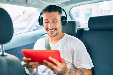 Genç İspanyol adam mutlu bir şekilde gülümsüyor. Arabada dokunmatik ped ve kulaklık kullanıyor..