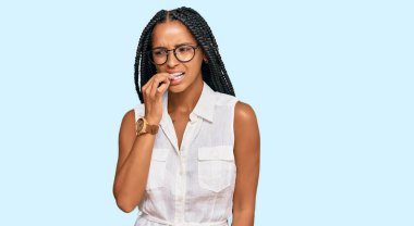 Gündelik kıyafetler ve gözlük takan güzel İspanyol kadın gergin görünüyor ve elleri ağızda tırnak yiyor. anksiyete. 