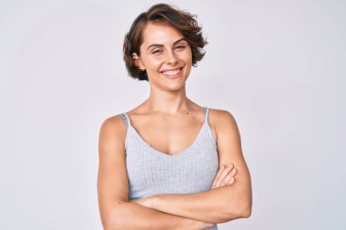 Gündelik kıyafetler giyen, kollarını kavuşturup kameraya gülümseyen genç İspanyol kadın. pozitif kişi. 