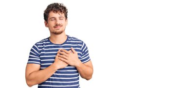 Kıvırcık saçlı, sıradan kıyafetler giyen, göğsünde elleri kapalı, yüzünde minnet ifadesi olan genç yakışıklı bir adam. sağlık kavramı. 