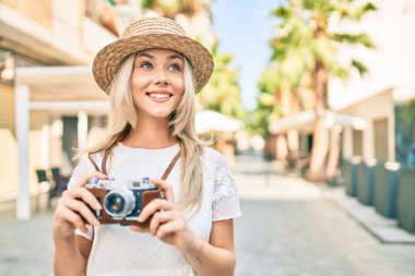 Beyaz tenli genç turist kız şehrin caddesinde klasik kamera kullanarak mutlu bir şekilde gülümsüyor..