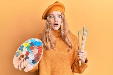 Güzel beyaz kız elinde boya fırçası ve ressam paleti tutarken şaşkınlık ve şaşkınlık içinde bir ifade, korku ve heyecan dolu bir yüz vardı.. 