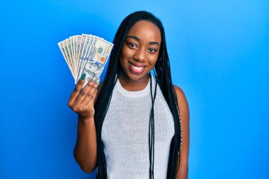 Genç Afro-Amerikalı kadın elinde dolarlar tutarken pozitif ve mutlu görünüyor. Kendine güvenen bir gülümsemeyle dişlerini gösteriyor. 