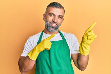 Orta yaşlı, daha temiz önlük giyen, eldivenli, gülümseyen ve kameraya bakan yakışıklı bir adam.. 