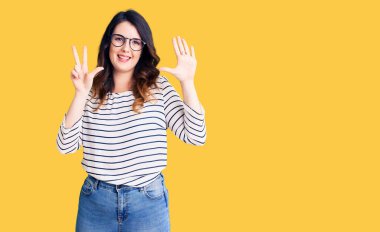 Güzel, genç, esmer bir kadın, günlük kıyafetler ve gözlük takıyor. Sekiz numaralı parmaklarıyla gösteriyor ve işaret ediyor. Kendinden emin ve mutlu gülümsüyor.. 