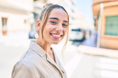 Genç, güzel, sarışın, beyaz bir kadın güneşli bir günde mutlu bir şekilde gülümsüyor.