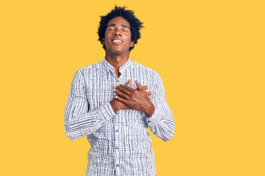 Yakışıklı Afro saçlı, sıradan kıyafetler giyen, göğsünde elleri kapalı, yüzünde minnet dolu bir jest olan Afro-Amerikan erkeği. sağlık kavramı. 