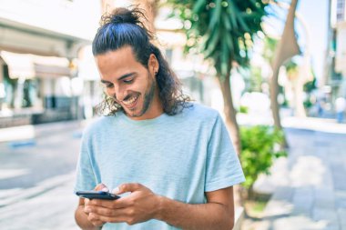 Genç İspanyol adam şehirde akıllı telefon kullanarak mutlu gülümsüyor..