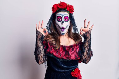 Ölü kostümü giymiş genç bir kadın beyazın üzerine şaşırmış ve şok olmuş görünüyor. Tamam sembolünü parmaklarıyla yapıyor. çılgın ifade 