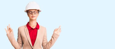 Mimar şapkası takan genç ve güzel bir kadın rahatla ve gülümse gözleri kapalı parmaklarıyla meditasyon hareketi yapıyor. yoga konsepti. 