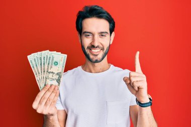 Elinde 20 dolarlık banknot tutan genç İspanyol bir adam bir fikir veya soruyla gülümsüyor ve mutlu bir yüzle işaret ediyor. 