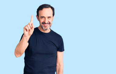 Orta yaşlı yakışıklı bir adam gündelik tişört giyer ve bir numaralı parmağını göstererek gülümserken kendinden emin ve mutlu olur.. 