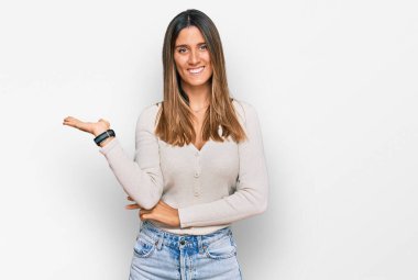 Gündelik giysiler giymiş neşeli bir şekilde gülümseyen ve avuç içi kameraya bakan genç bir kadın.. 