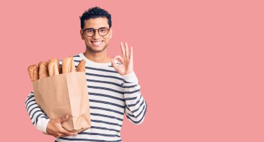 İspanyol asıllı yakışıklı, elinde ekmek torbası olan genç adam parmaklarıyla imza atıyor, gülümseyerek mükemmel bir sembol oluşturuyor. 